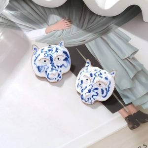 Close-up of blue and white enamel tiger earrings with intricate gold-plated metal borders