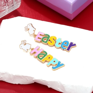 Macro shot of asymmetric Easter earrings with white bunnies and colorful enamel letters