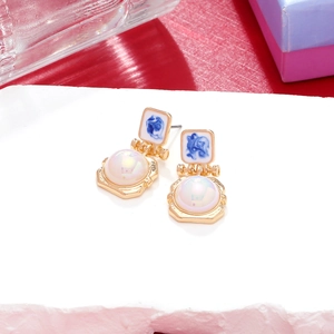 Detail of vintage gold-plated earrings with blue enamel and iridescent pearl accents