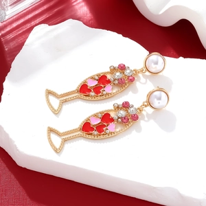 Close-up of golden champagne glass earrings with pink heart patterns and pearls