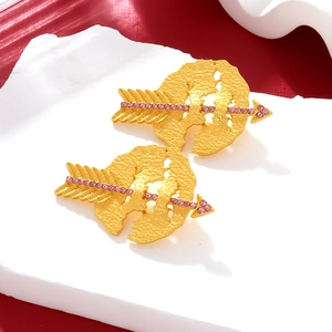 Macro detail of Cupid arrow earrings with pink rhinestones on a gold textured disk