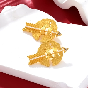 Golden Cupid's arrow earrings with hammered texture and faux pearls on red background