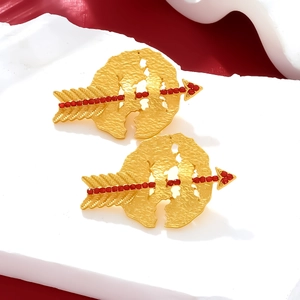 Detailed view of gold Cupid arrow earrings with red beads and textured finish