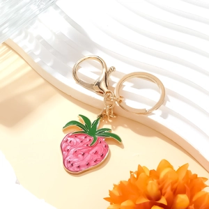 Cute strawberry enamel keychain with gold clasp on a minimalist white wavy stand