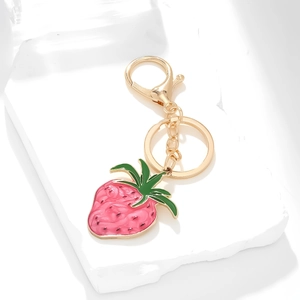 Pink enamel strawberry keychain with gold metal lobster clasp on a white stone base