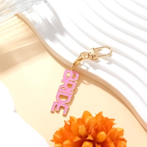 Pink enamel BRIDE letter keychain with gold metal finish on white decorative platform