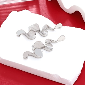 Detail of silver wavy fluid drop earrings displayed on a white stone pedestal with red background