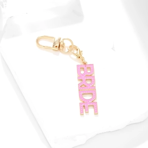 Pink enamel BRIDE letter keychain with golden lobster clasp on white marble base