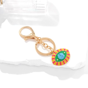 Golden Evil Eye keychain with colorful enamel inlay and blue crystal on stone background
