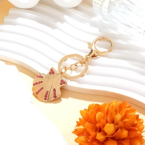 Golden shell keychain with pink rhinestones and lobster clasp on white wavy stand