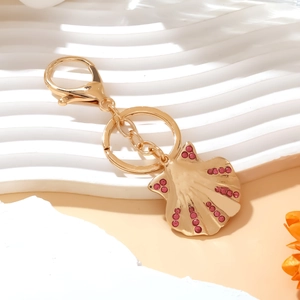 Golden shell keychain pendant with pink rhinestones on a decorative white display