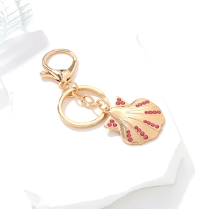 Gold seashell keychain with pink rhinestones on a white marble display stand