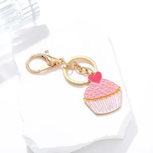Pink pearl cupcake keychain with heart charm and golden lobster clasp on white stone