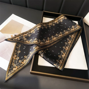 Élégant foulard en soie noir et or à motif paisley présenté sur un plateau de luxe