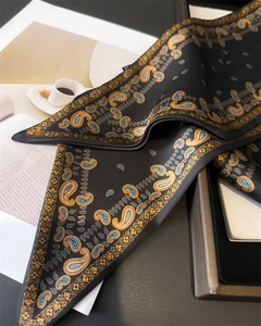 Détail d'un foulard en soie paisley avec motifs dorés et bleus sur tissu noir