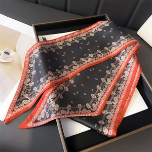 Détail d'un foulard en soie noir à motif paisley avec bordure orange sur un plateau