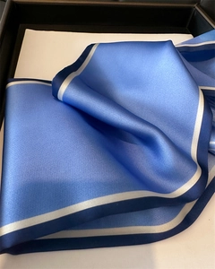 Close-up of blue satin silk scarf with white stripes folded neatly in a black gift box
