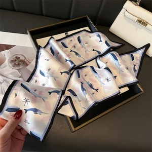 Detail view of a long narrow silk scarf with blue whale prints and soft pink accents