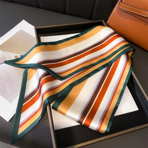 Twilly en soie à rayures géométriques colorées présenté sur un fond de sac en cuir de luxe