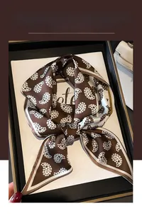 Detail of a dark brown paisley silk-like scarf neatly knotted inside a black gift box