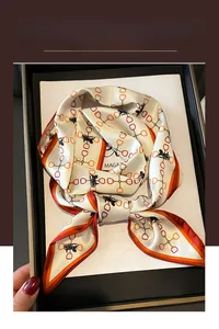 Détail d'un foulard en soie avec motif carrosse et chaîne dans un coffret cadeau noir