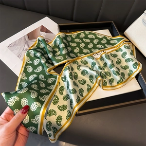 Detail of a green and white paisley silk twilly scarf with yellow borders on a leather tray