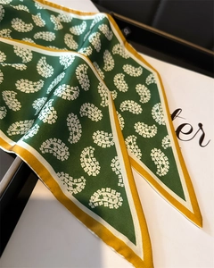 Detail of a dark green paisley twilly scarf with yellow borders on a white box