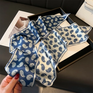 Detail view of a luxury navy and beige paisley silk scarf on a stylish display tray