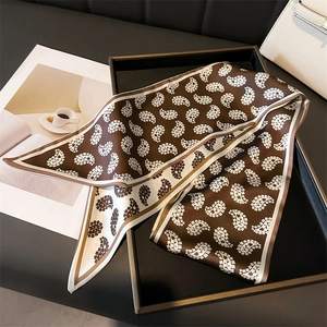 Close-up of brown and cream paisley skinny scarf neatly folded in a premium display box