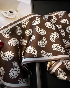 Close-up of silk-like paisley pattern scarf displayed on a luxury packaging box