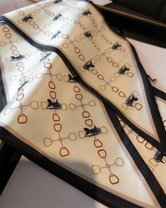 Détail d'un foulard en soie avec motif de calèche et chaîne sur tissu beige élégant