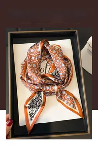 Détail d'un foulard en soie orange vif avec motifs floraux dans un coffret cadeau