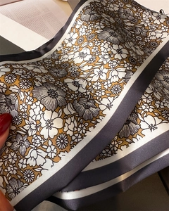 Détail d'un foulard en soie jaune moutarde avec motif floral rétro et bordure gris foncé