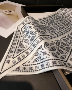 Detailed view of paisley ivory silk scarf with elegant black patterns on a tray