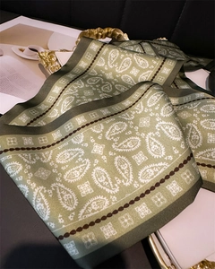 Macro detail of silk scarf featuring white paisley pattern on dark green fabric