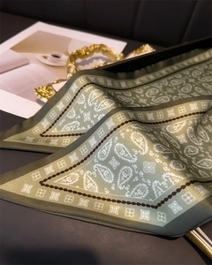 Close-up of green silk paisley scarf with a sleek satin texture on a gold metal tray
