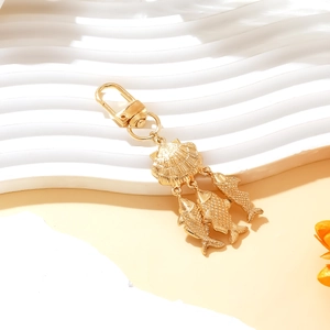 Golden ocean style keychain with sea shell pendant and dangling fish charms on white wave base