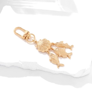 Golden keychain with ocean shell and fish pendants on a minimalist white stone surface
