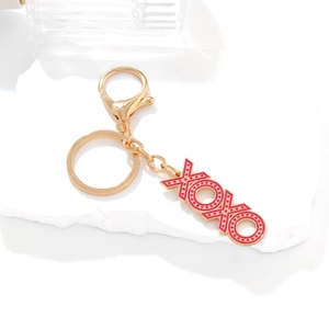 Golden XOXO keychain with red enamel and pink dots on white display stone pedestal