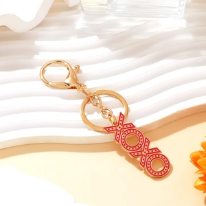 Gold keychain with red enamel XOXO pendant featuring white dots on a wave stand