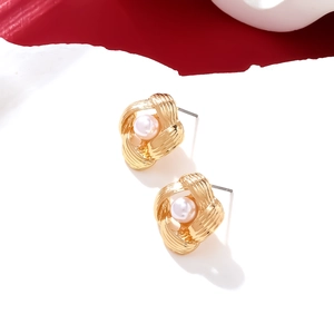 Detail view of twisted gold knot stud earrings with white pearl center on white surface