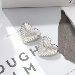 Macro detail of silver heart earrings featuring textured vertical stripes on alloy metal