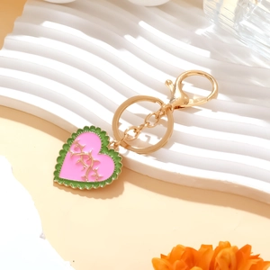 Pink heart enamel keychain with green wavy borders and golden lobster clasp on a display stand