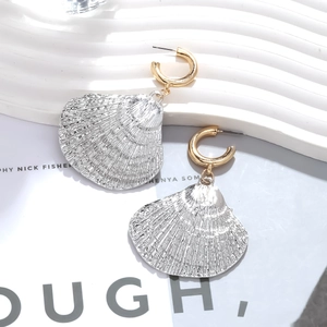Macro detail of golden C-shaped hook earrings with silver shell charms and textures