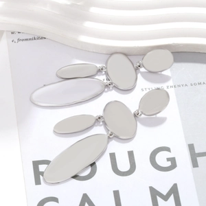 Close-up of long silver geometric alloy earrings with polished oval plates on a magazine