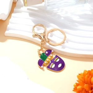 Circus clown mask keychain with purple enamel and pearls on white textured background