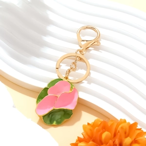 Pink and green flower enamel keychain with golden clip on a white textured stand