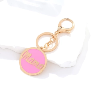 Pink enamel Mama charm keychain with gold lettering and lobster clasp on marble stand