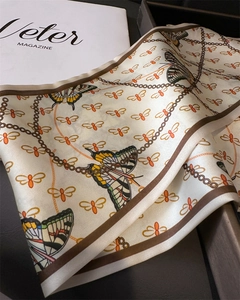 Detail of silk-like scarf featuring colorful butterfly patterns and gold chain texture