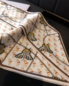 Close-up of silk-textured scarf with butterfly and chain patterns in elegant box